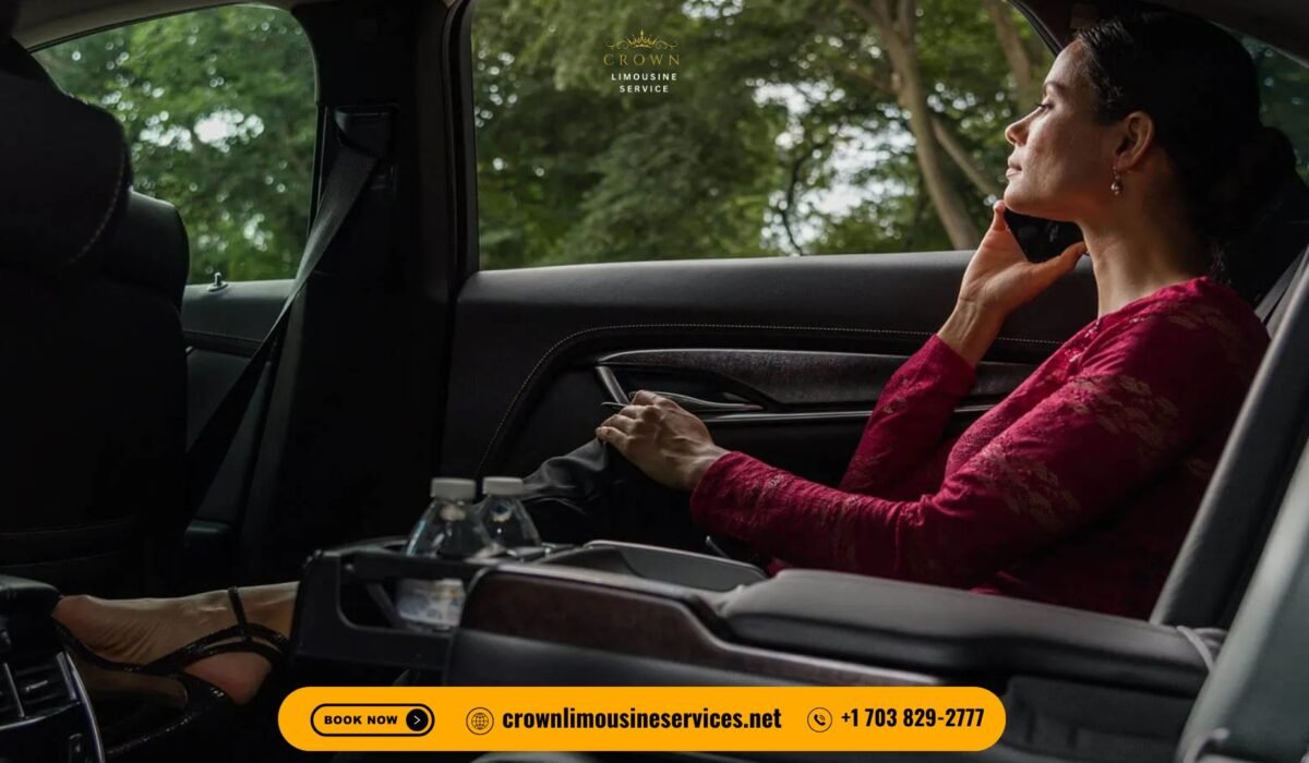 Passenger seated in the back of a luxury Crown Limousine, speaking on the phone, with premium leather seating, bottled water in the console, and company branding visible, trees outside the window.